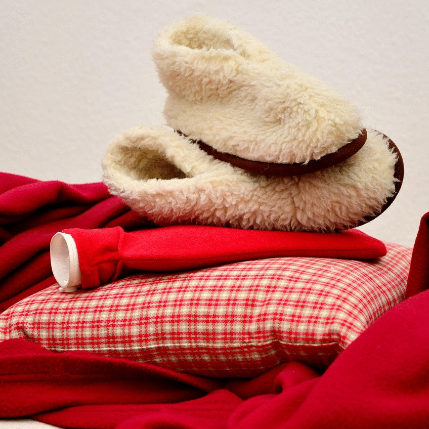 Blanket with a pillow and hot water bottle, with a pair of slippers on top